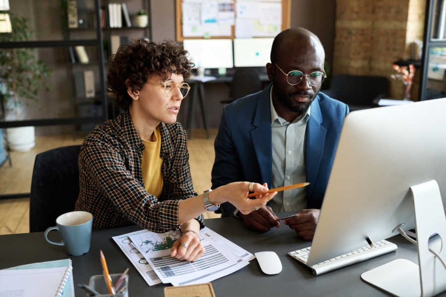 Businesswoman pointing at computer monitor and discussing presentation together with her colleague at at office