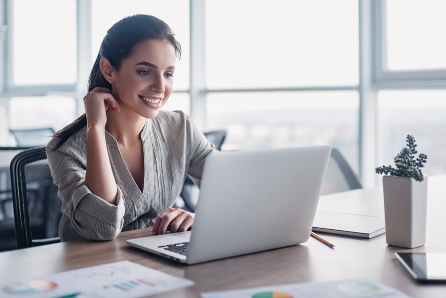 Portrait of gorgeous, smiling young female using laptop computer at workplace